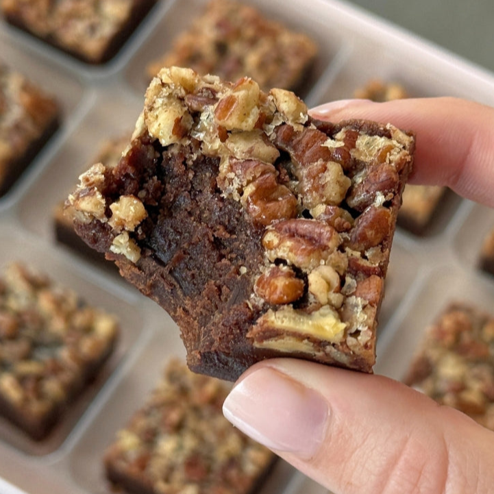 Brownie with pecans held above a tray of brownies