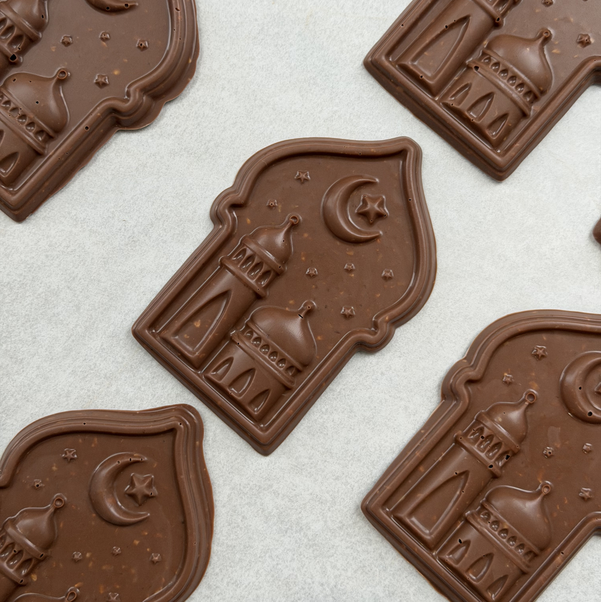 Golden Crescent milk chocolate plaques with mosque and crescent moon designs laid out on baking paper