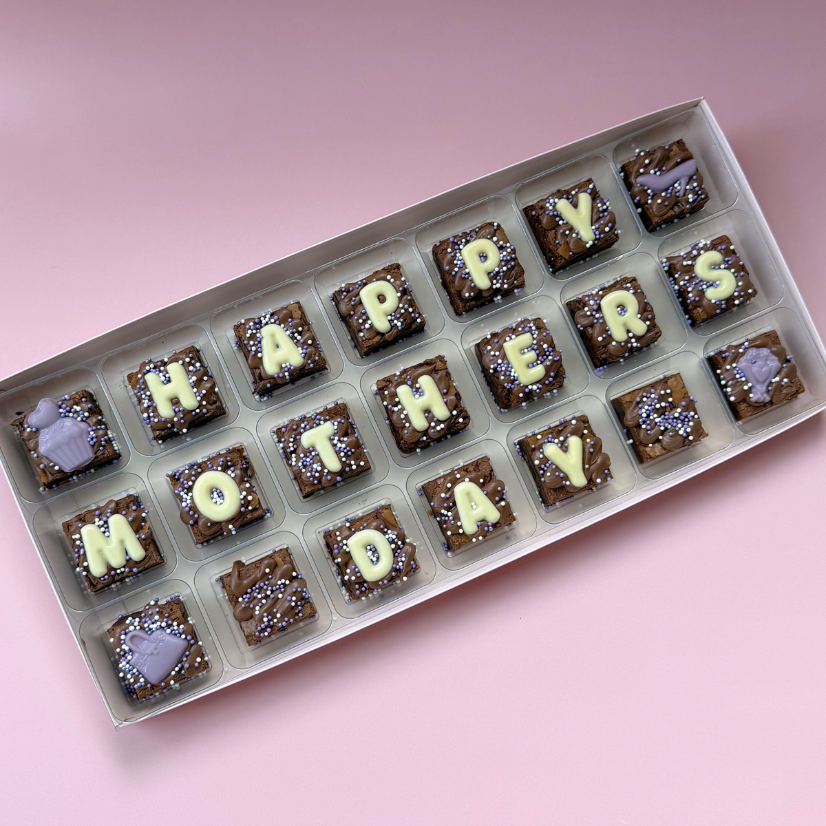 Box of 21 mini brownies spelling "Happy Mother's Day" in white chocolate letters with lilac toppers