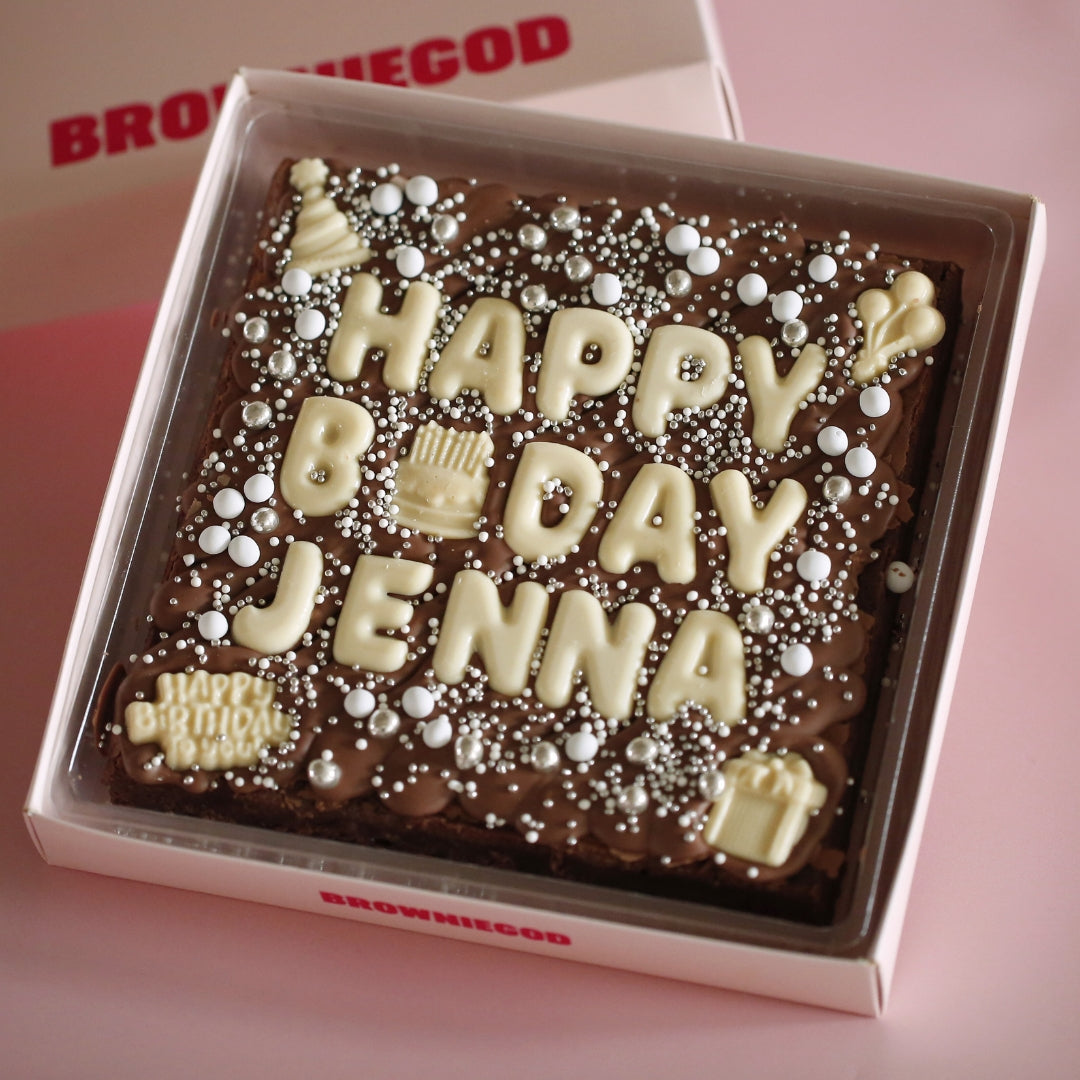 Brownie slab spelling "Happy bday Jenna" in white chocolate letters, with silver sprinkles and white chocolate birthday icons
