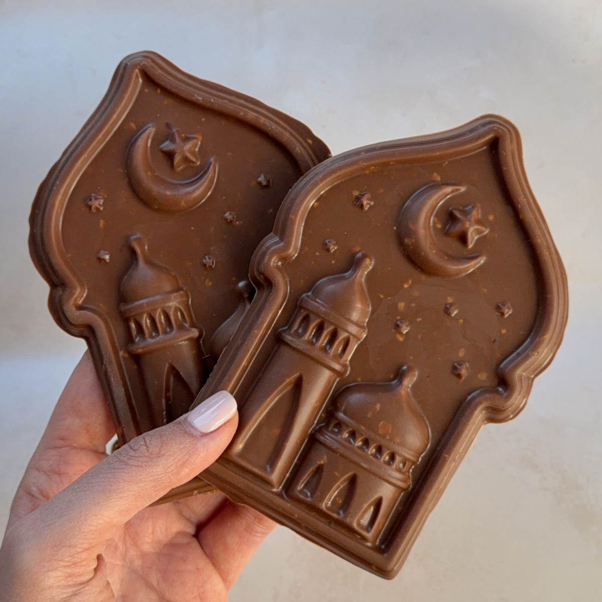 Hand holding two Golden Crescent chocolate plaques moulded with a mosque, crescent moon and stars
