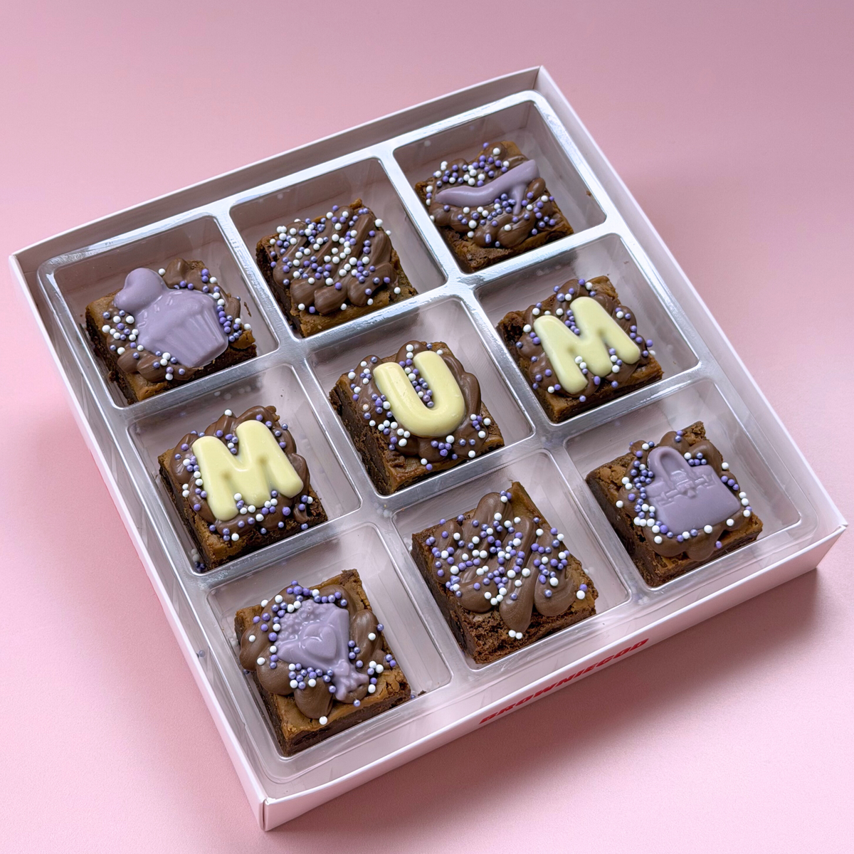 Box of nine Mother's Day mini brownies with "Mum" in white chocolate letters, lilac sprinkles and lilac chocolate handbags