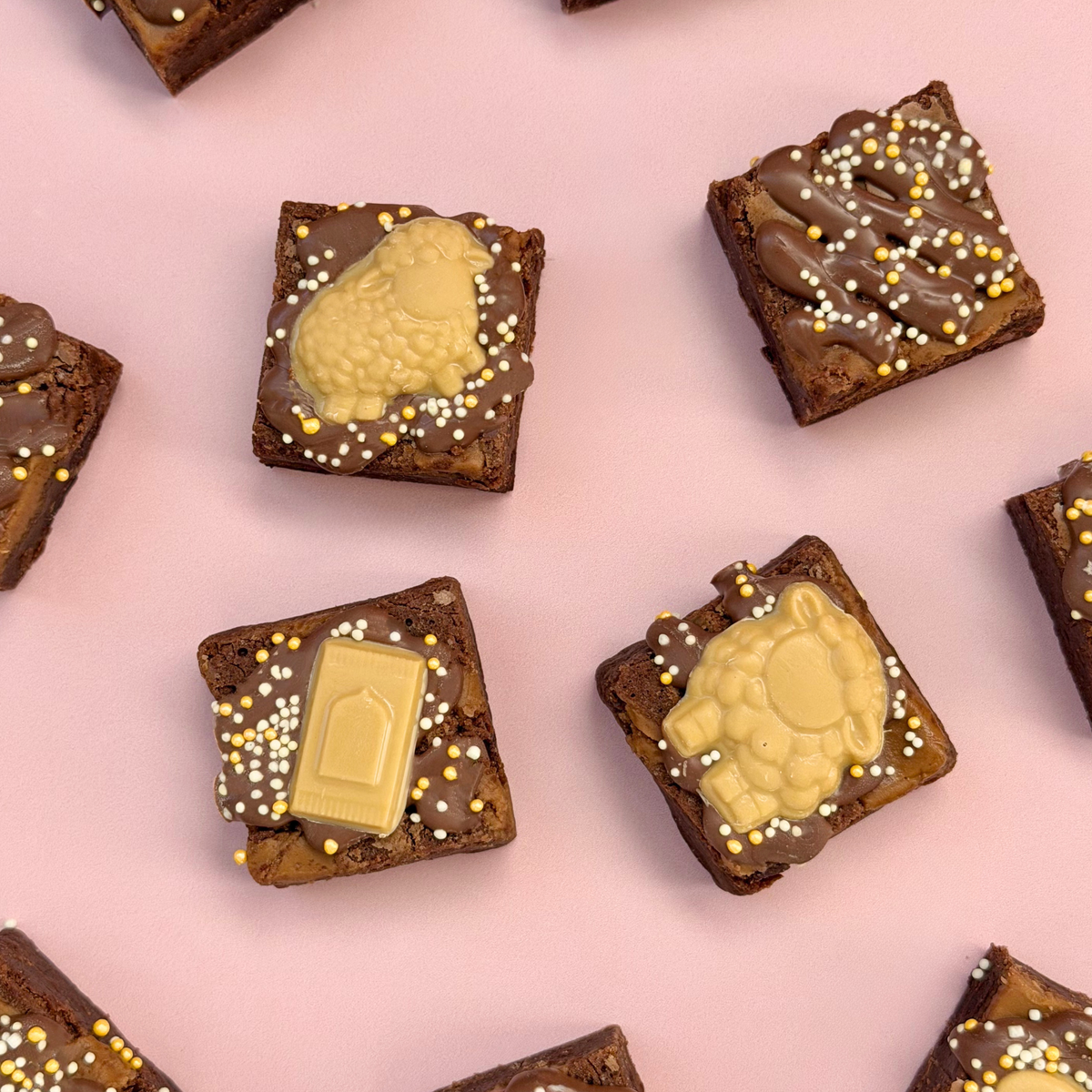 Overhead of Eid mini brownies topped with gold chocolate sheep and milk carton toppers on a pink background