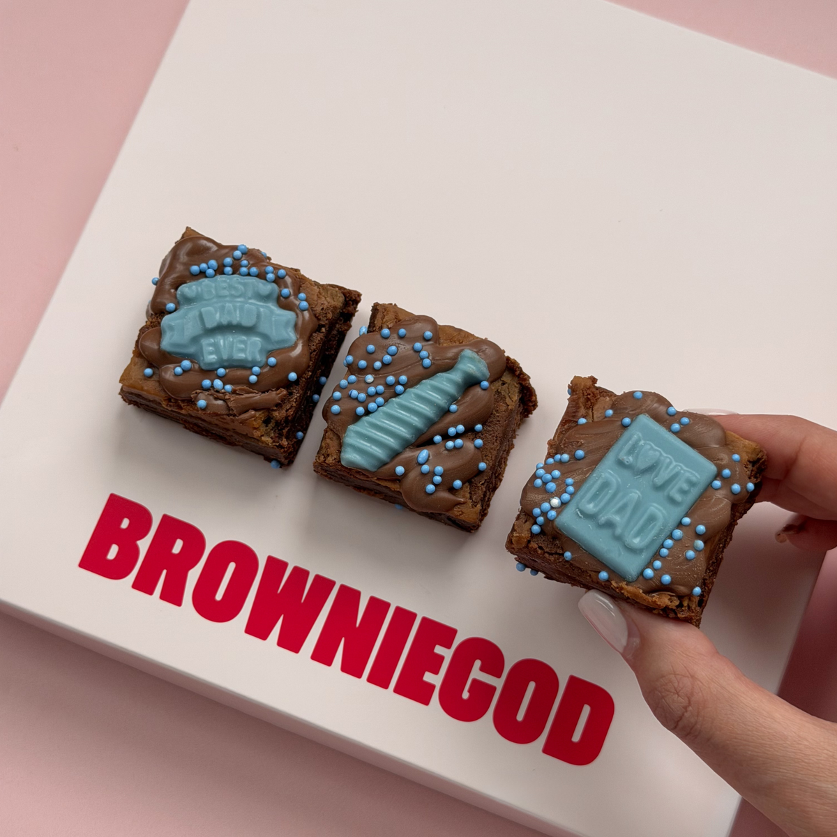 Hand holding one of three Father's Day mini brownies with blue chocolate "best dad ever" badge, tie and "love dad" toppers