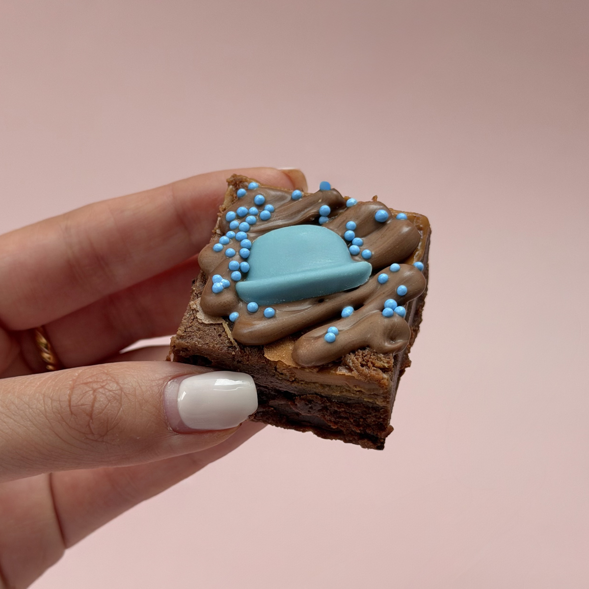 Hand holding a Father's Day brownie topped with a blue chocolate bowler hat and blue sprinkles