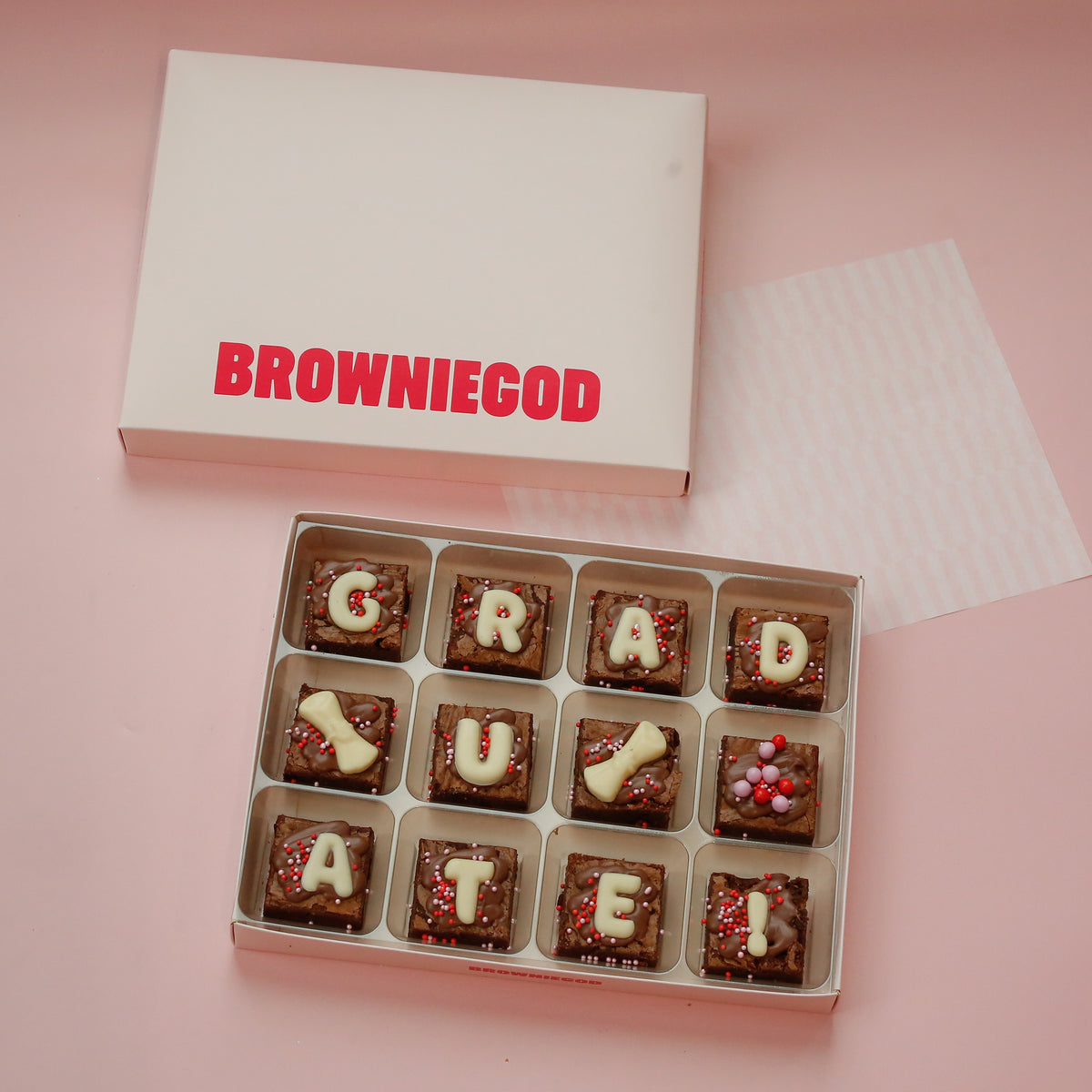 Box of 12 mini brownies spelling "Graduate!" in white chocolate letters, next to the Browniegod box lid