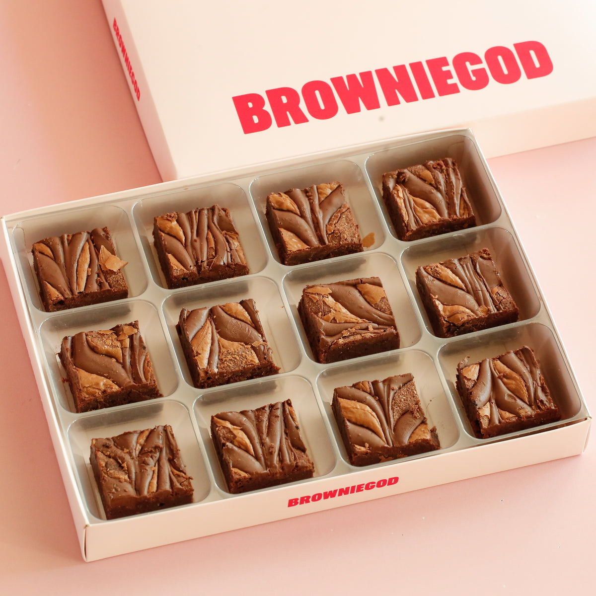 Box of 12 brownies with a chocolate spread swirl on top, next to the Browniegod box lid