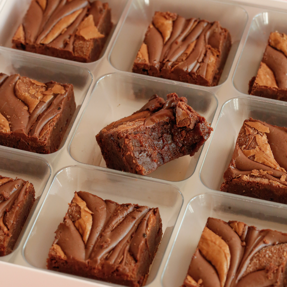 Close-up of swirl-topped brownies in a tray, one bitten to show the fudgy centre