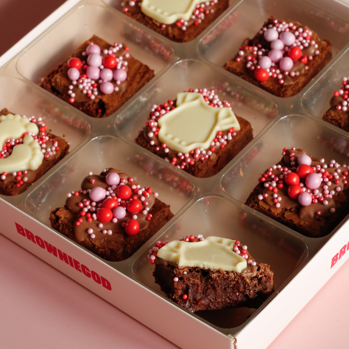 Close-up of baby mini brownies with white chocolate onesie and footprint toppers and pink and red sprinkles, one bitten