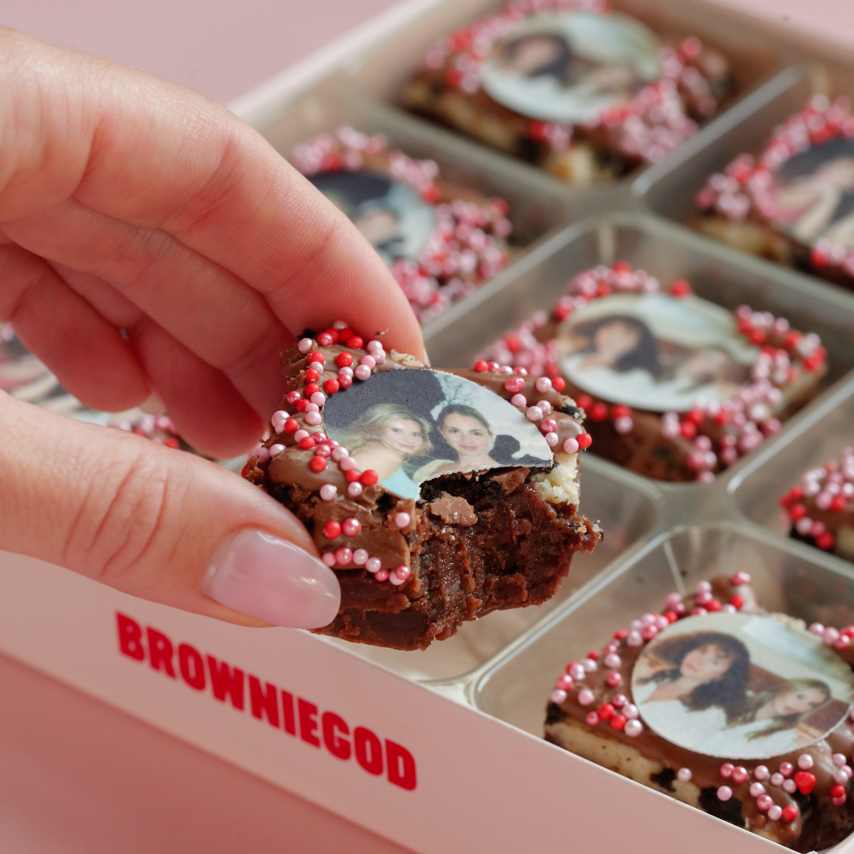 Hand holding a bitten photo brownie with a printed photo topper, above a box of photo brownies