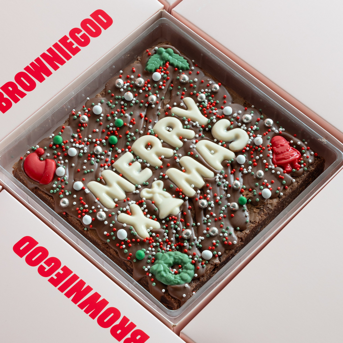 Christmas brownie slab reading "Merry Xmas" in white chocolate letters with red and green chocolate decorations and festive sprinkles