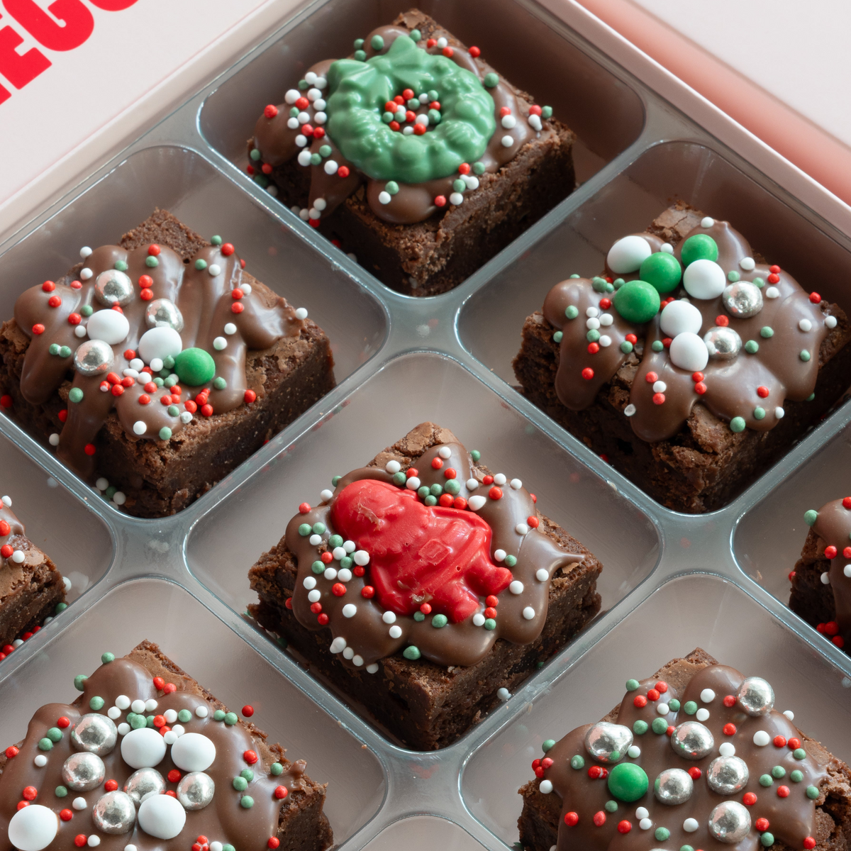 Close-up of Christmas mini brownies in a clear tray with a green chocolate wreath, a red Santa topper and silver and green sprinkles