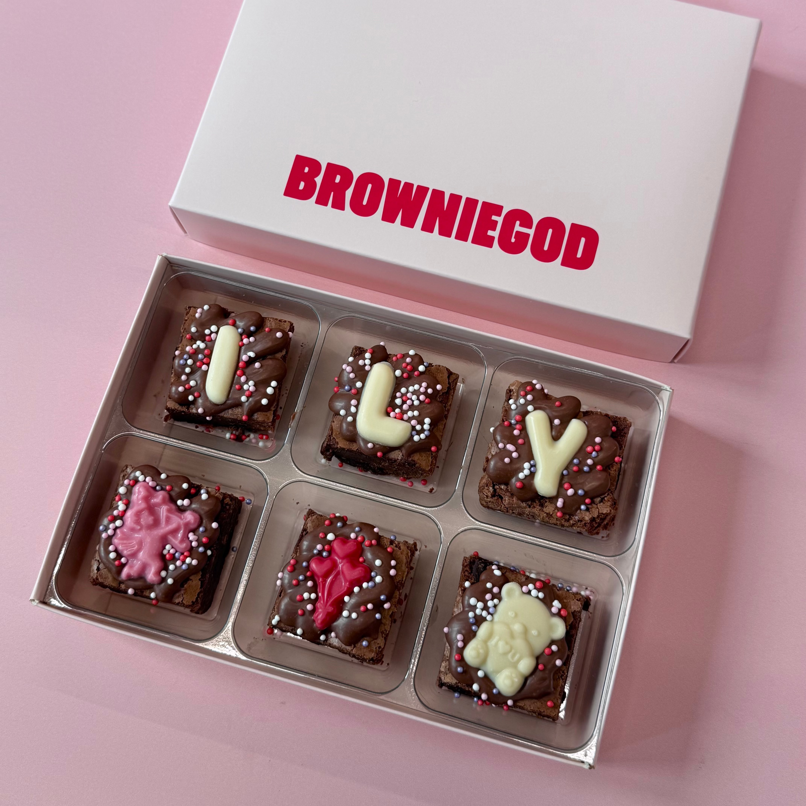 Box of six Valentine's mini brownies spelling "ILY" with pink chocolate cupid and teddy toppers, below the Browniegod box lid