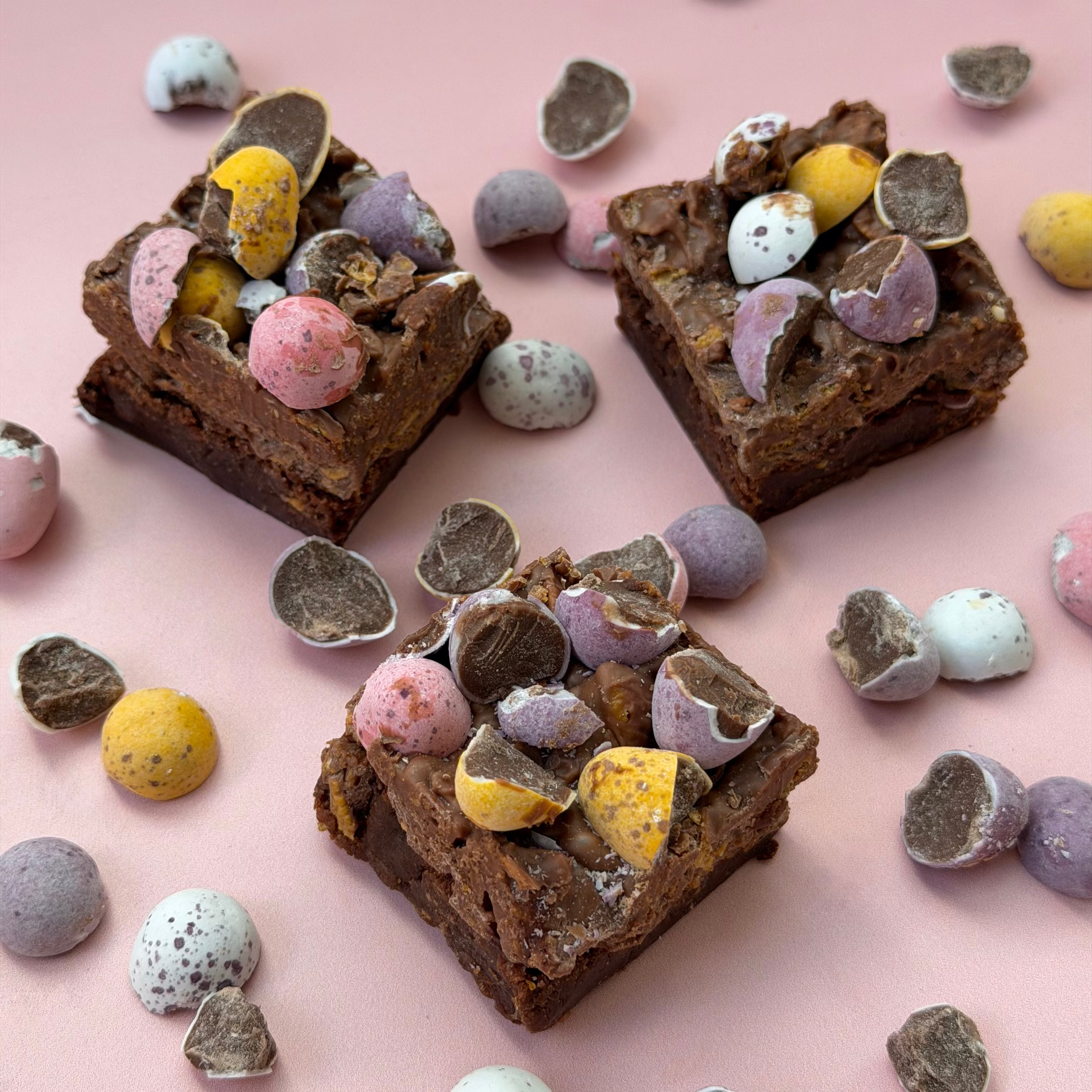 Chocolate brownies with colorful candy pieces on a pink background