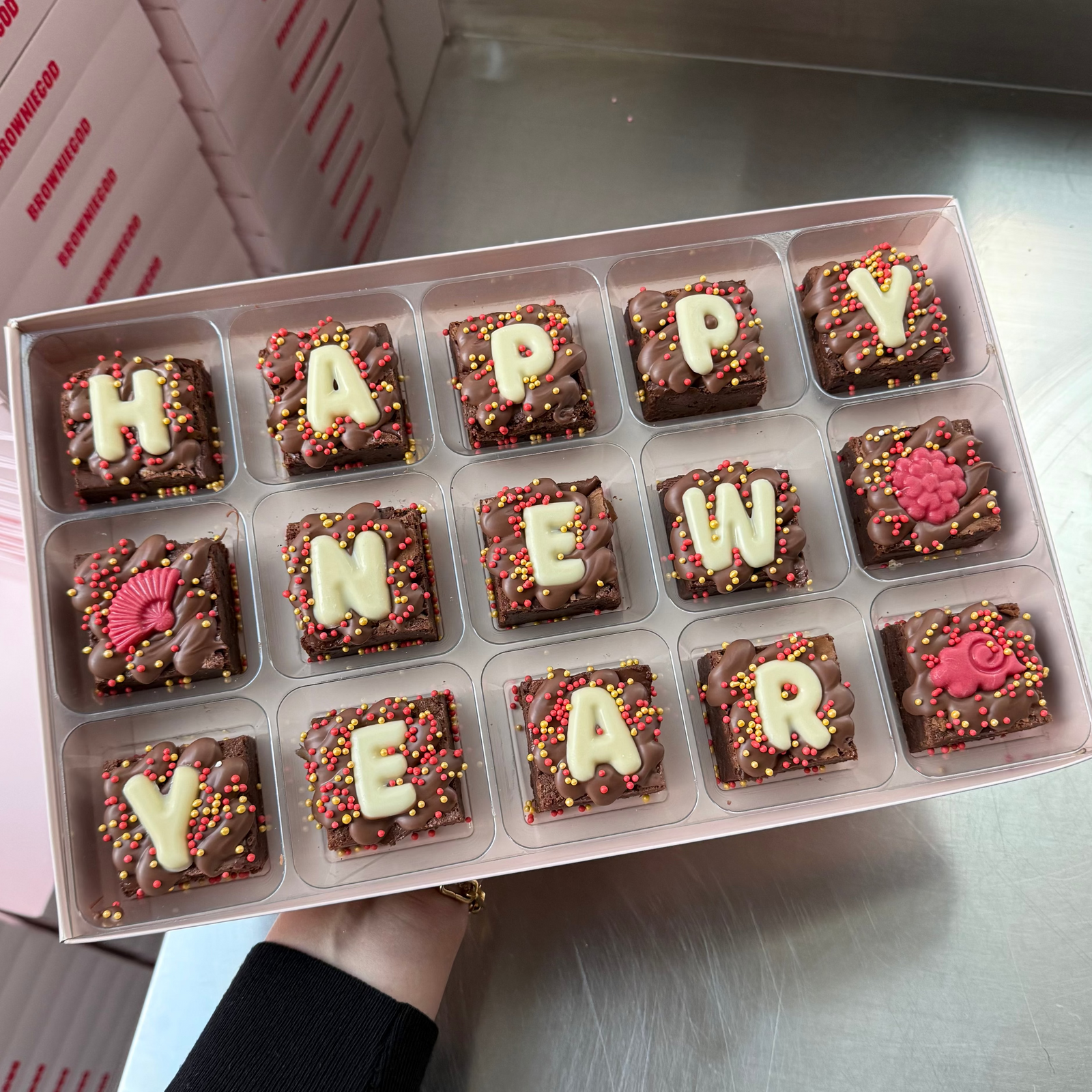 Box of 15 mini brownies topped with white chocolate letters spelling "Happy New Year" and red Lunar New Year toppers