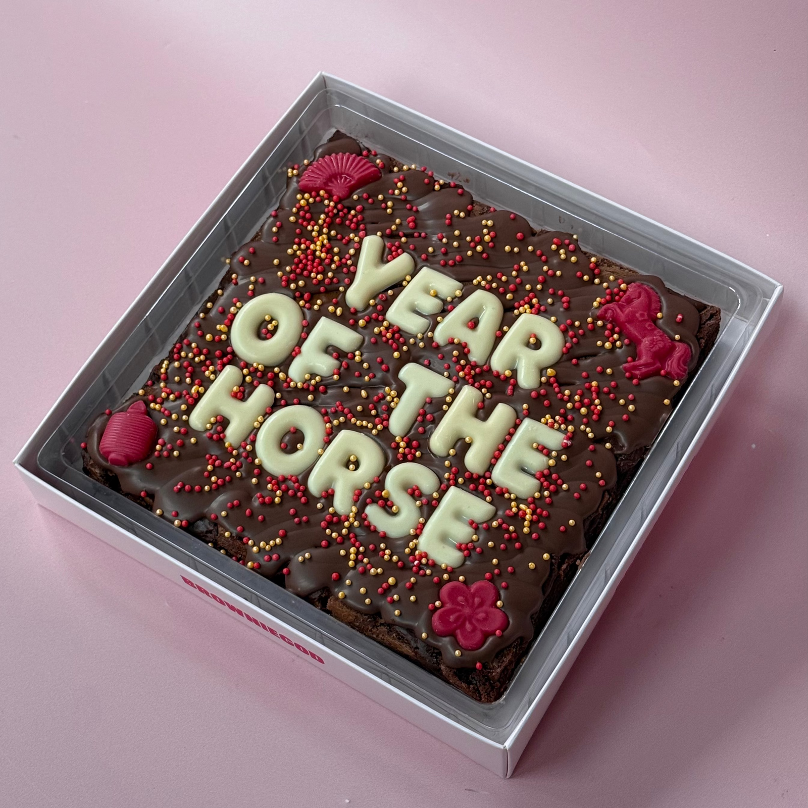 Chocolate brownie slab topped with white chocolate letters reading "Year of the Horse" and red Lunar New Year decorations