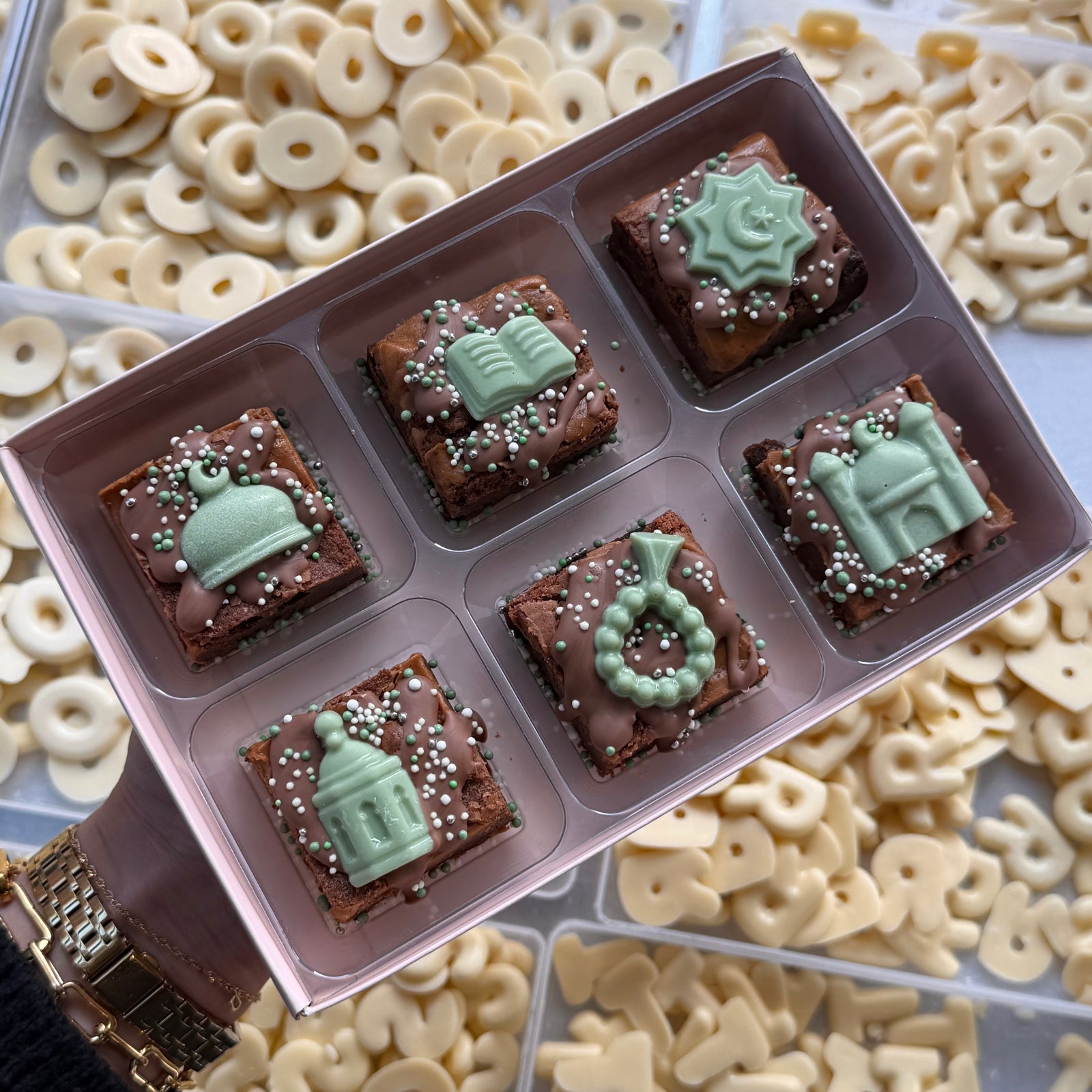 Hand holding a box of six Ramadan mini brownies with green chocolate mosque, book, lantern and crescent toppers
