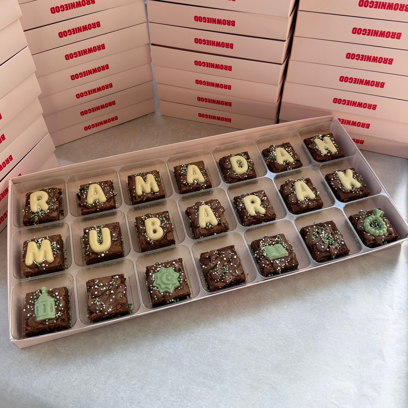 Box of 21 mini brownies spelling "Ramadan Mubarak" in white chocolate letters with green chocolate toppers