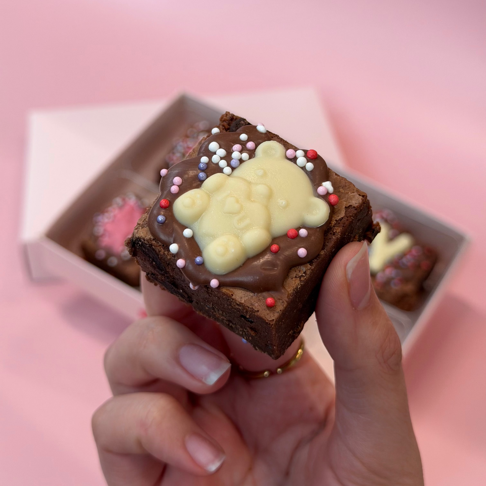 Hand holding a mini brownie topped with a white chocolate teddy bear and pastel sprinkles