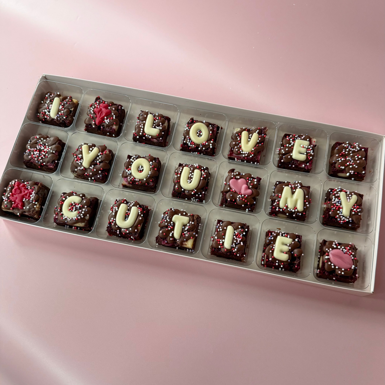 Box of 21 mini brownies spelling "I love you cutie" in white chocolate letters with pink chocolate toppers
