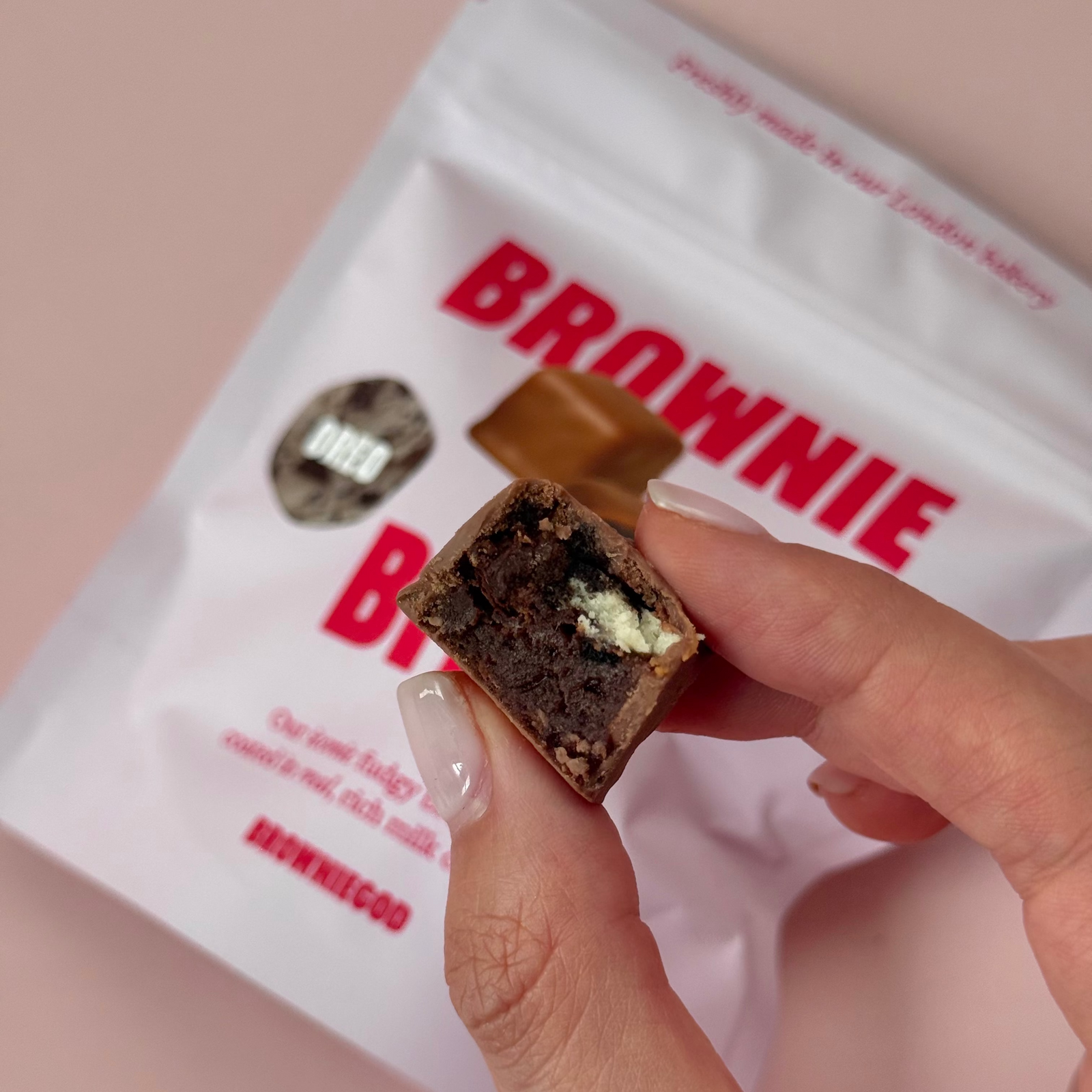 Hand holding a bitten Oreo cheesecake brownie bite in front of a Brownie Bites pouch