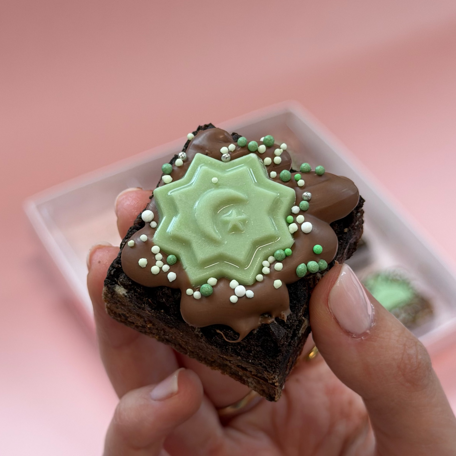 Hand holding a mini brownie topped with a green chocolate crescent and star and green sprinkles